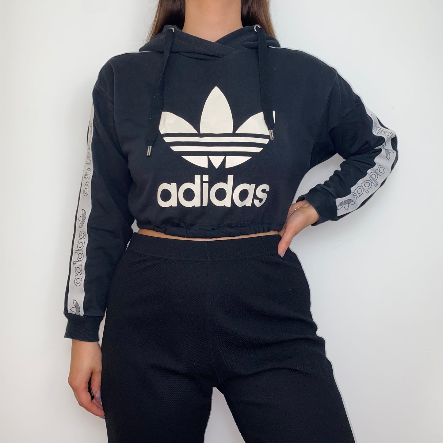 black cropped hoodie with white adidas logo shown on a model wearing black trousers