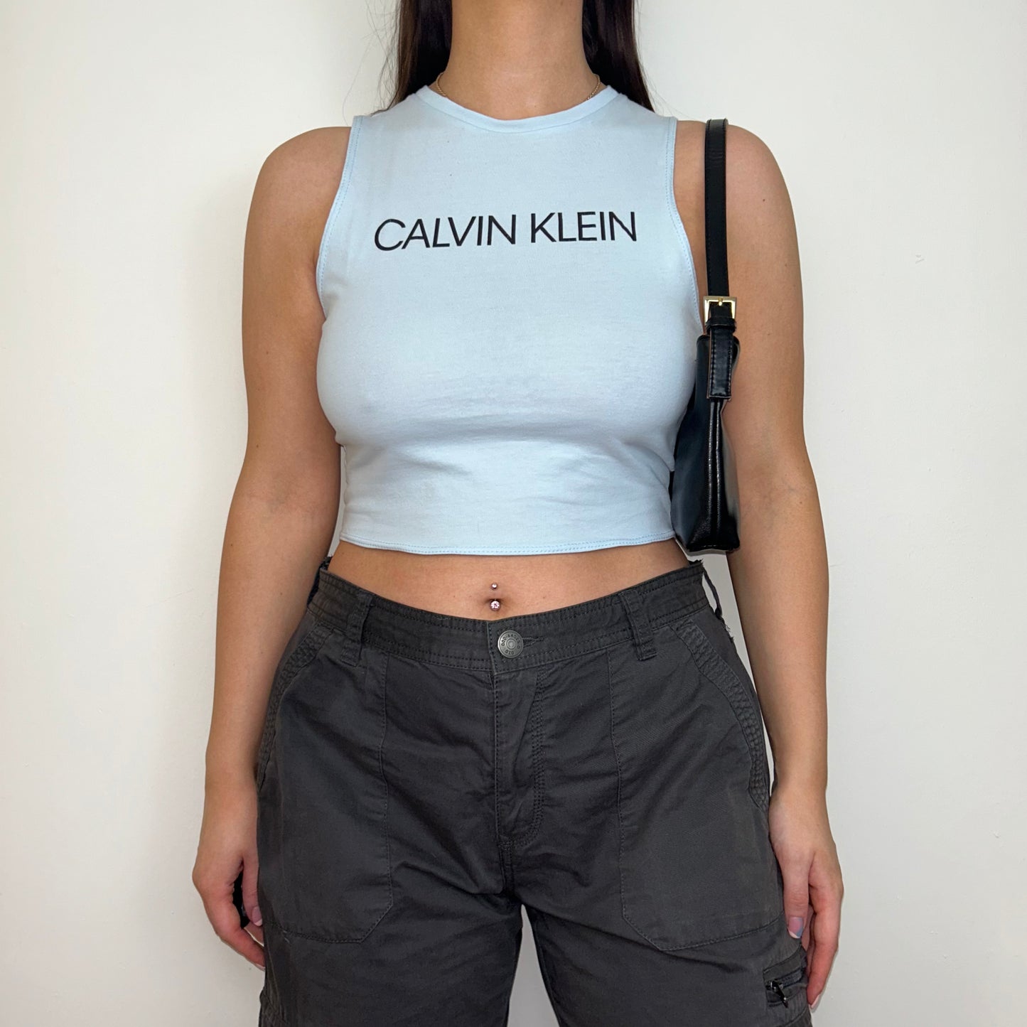 baby blue sleeveless crop top with black calvin klein logo shown on a model wearing grey cargo trousers and a black shoulder bag