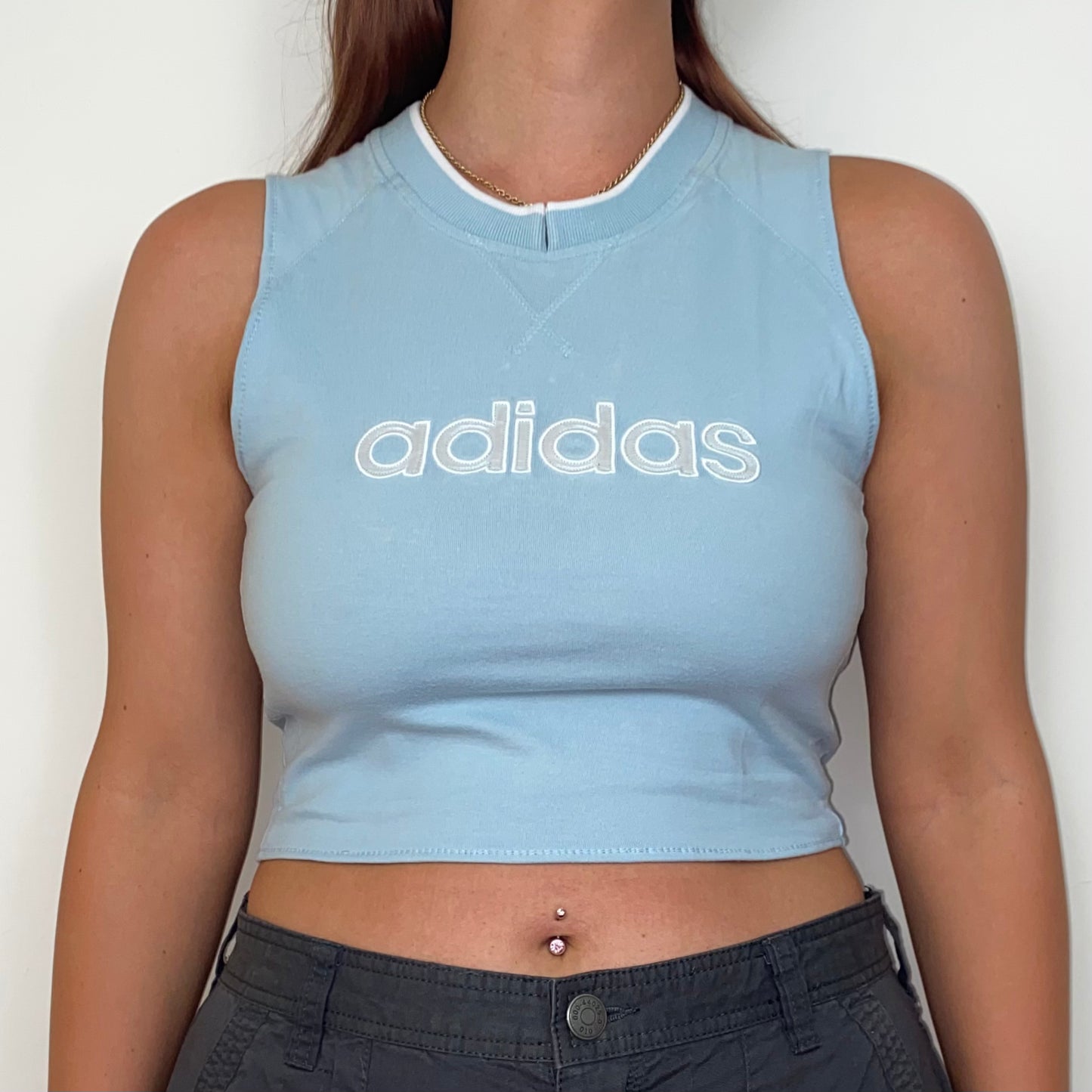 close up of a light blue sleeveless crop top with white adidas logo shown on a model wearing grey trousers