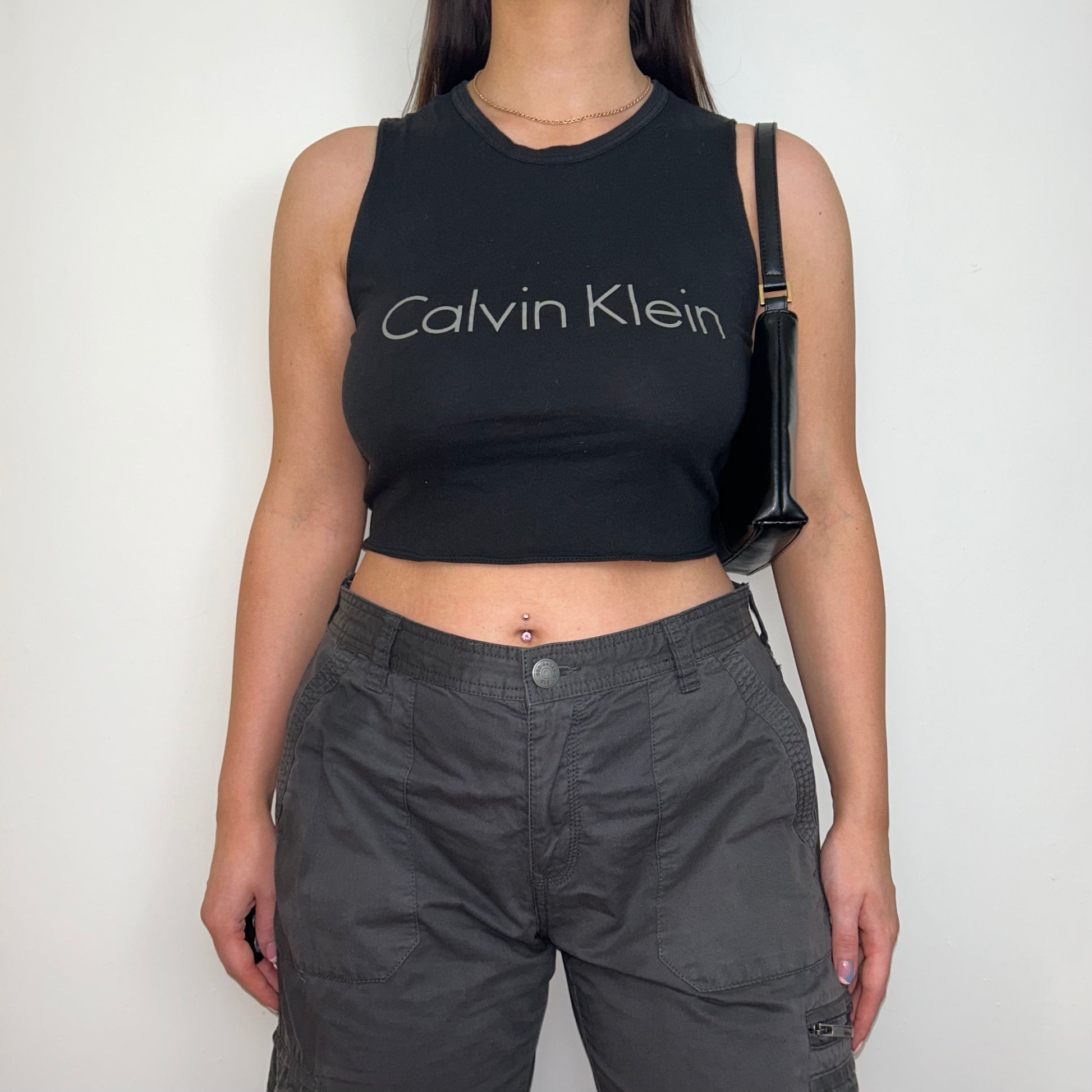 black sleeveless crop top with grey calvin klein logo shown on a model wearing grey cargo trousers and a black shoulder bag