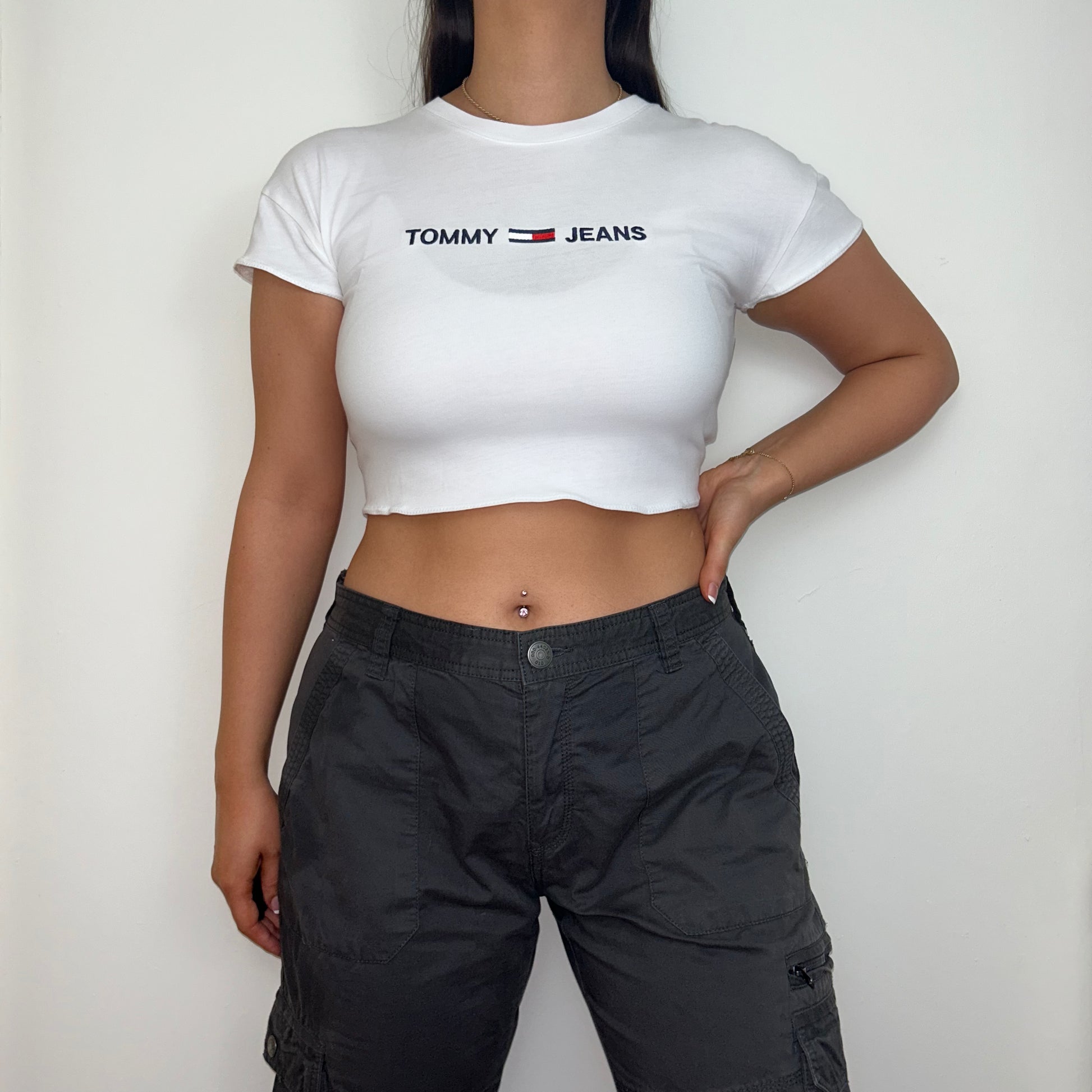 white short sleeve crop top with black tommy jeans logo shown on a model wearing cargo trousers