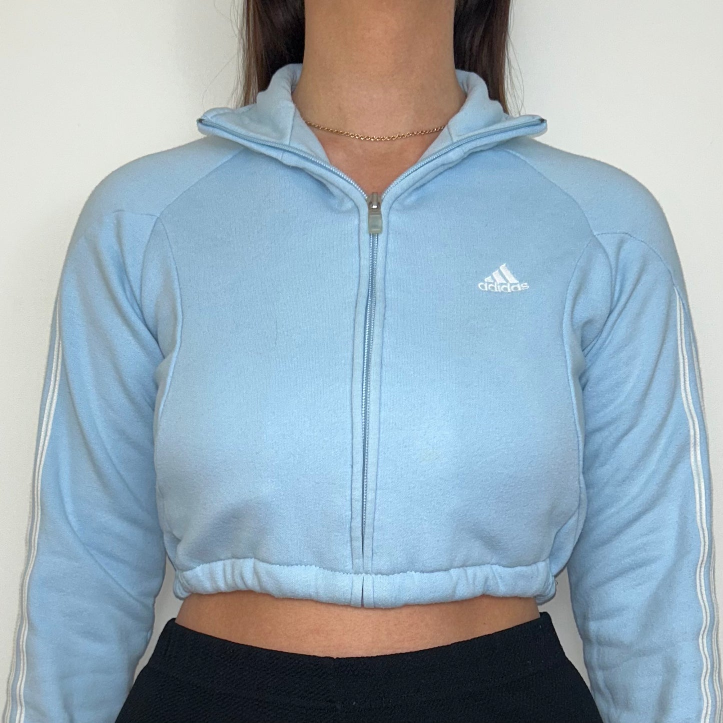 close up of light blue 1/4 zip cropped sweatshirt with white adidas logo shown on a model
