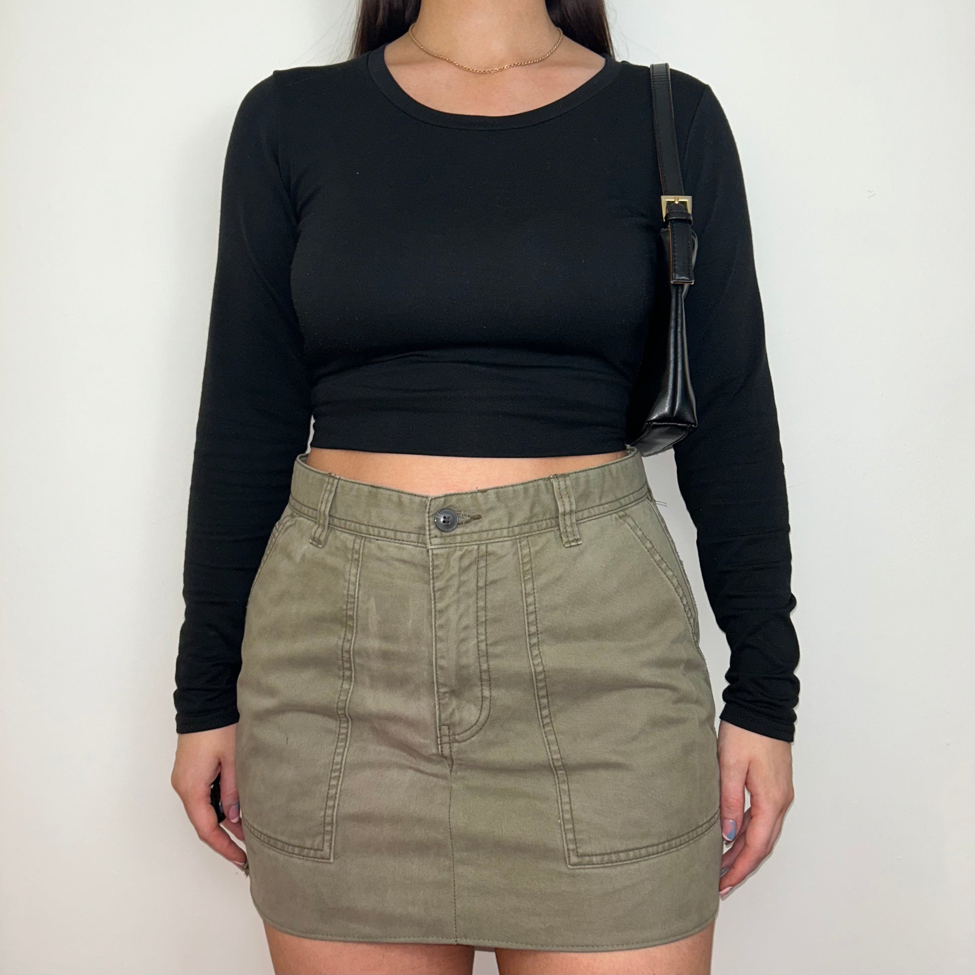 beige cargo mini skirt shown on a model wearing a long sleeve black top and a black shoulder bag