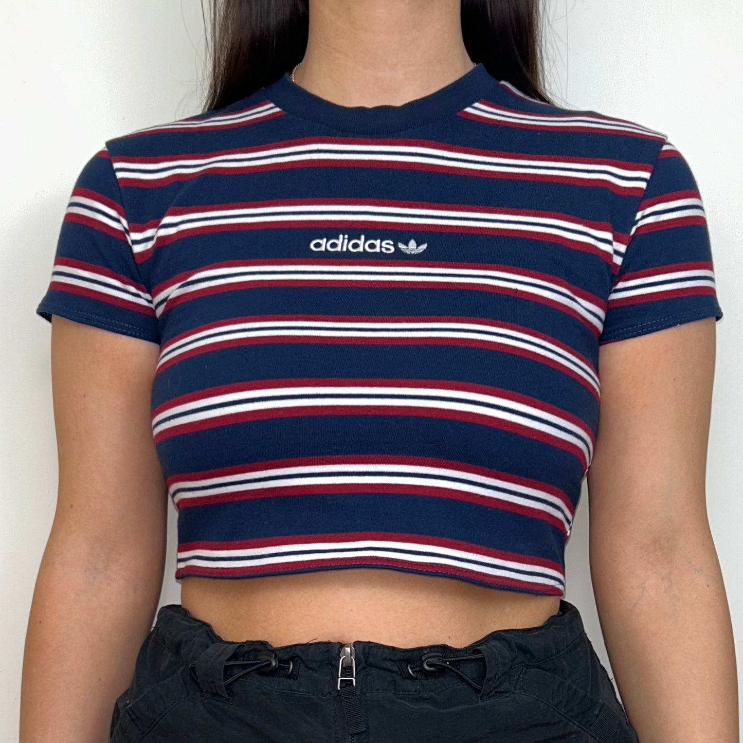 close up of navy and red short sleeve crop top with white adidas logo shown on a model wearing a black mini skirt
