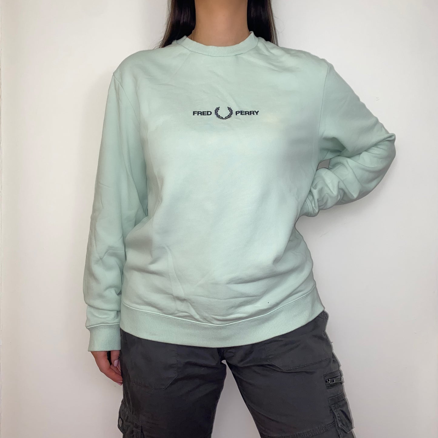 green sweatshirt with black fred perry logo shown on a model wearing grey cargo trousers
