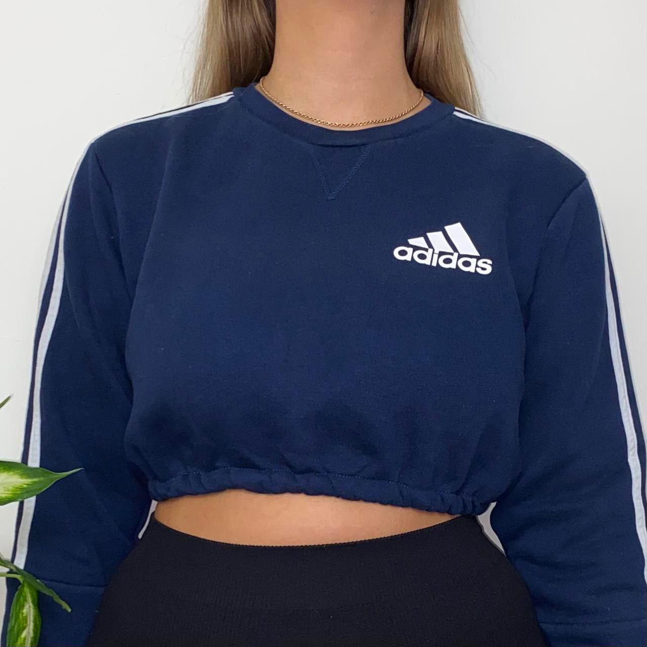 close up of navy sweatshirt with small adidas text and symbol logo on chest with white 3 stripes on arms shown on model