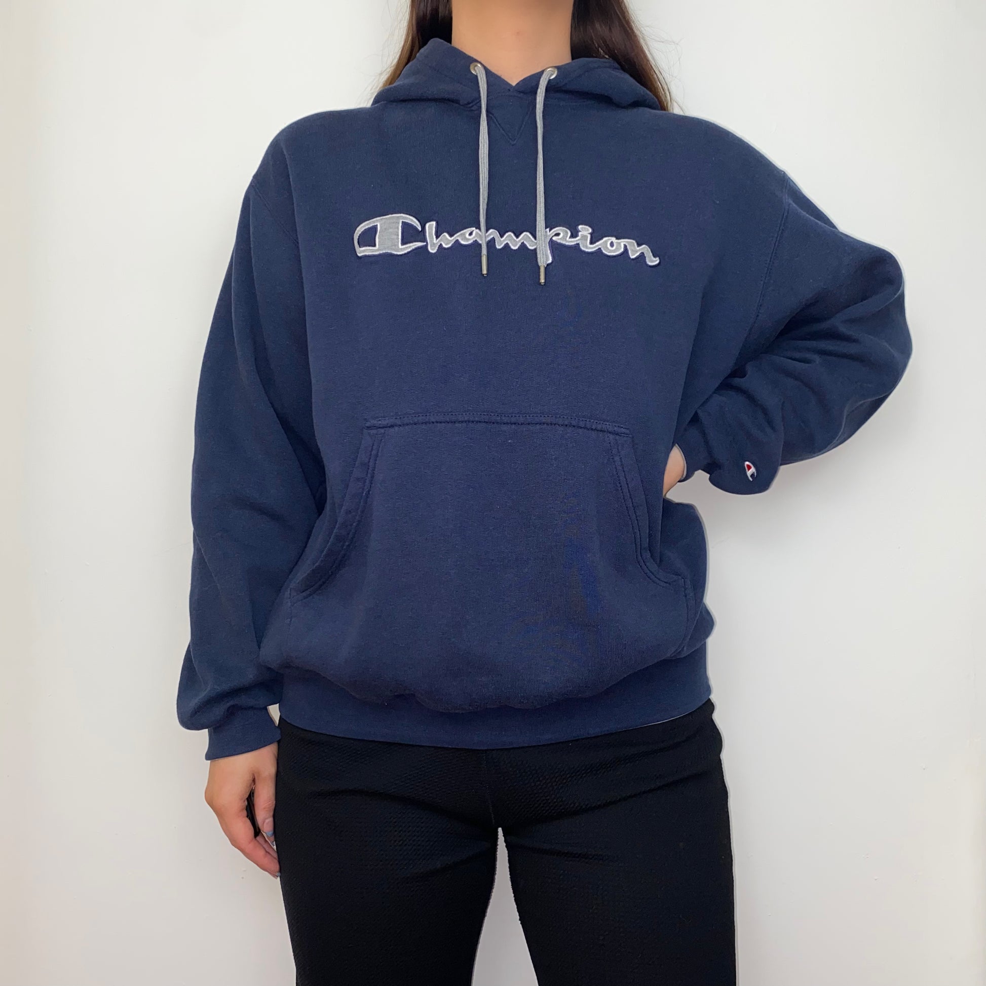 navy blue hoodie with big text champion logo shown on a model wearing black trousers