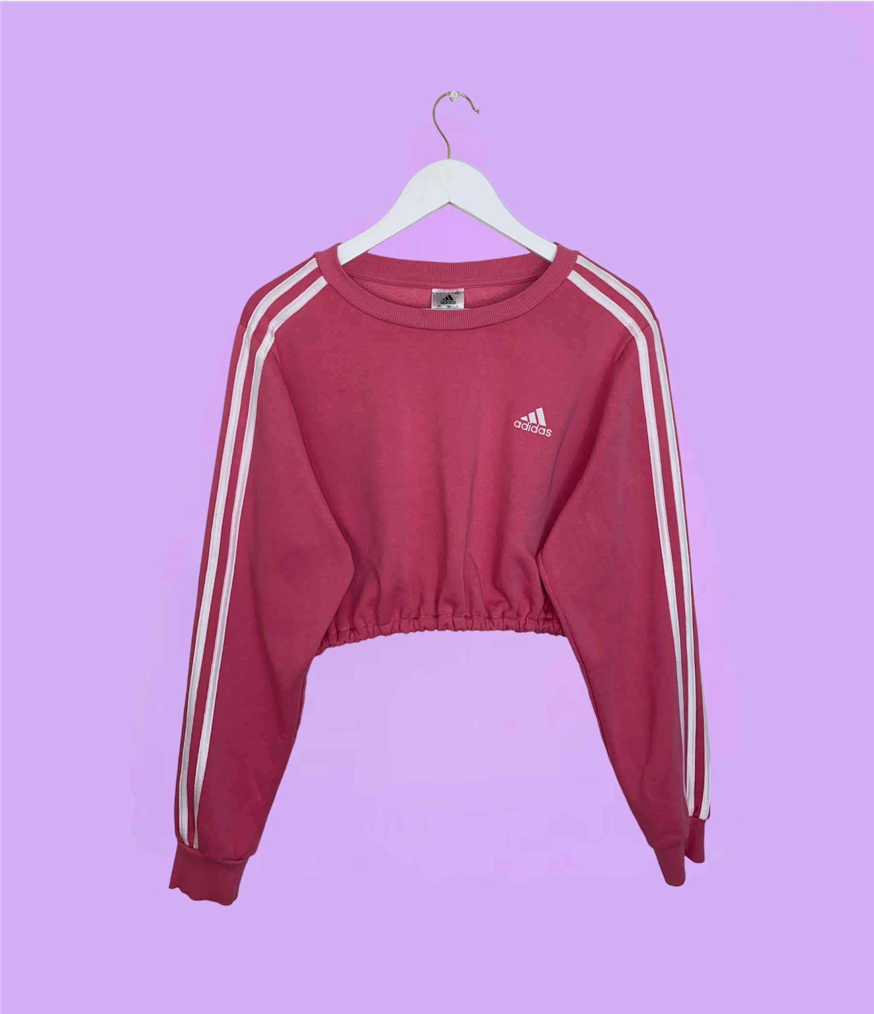 pink adidas cropped sweatshirt with white adidas logo shown on a lilac background