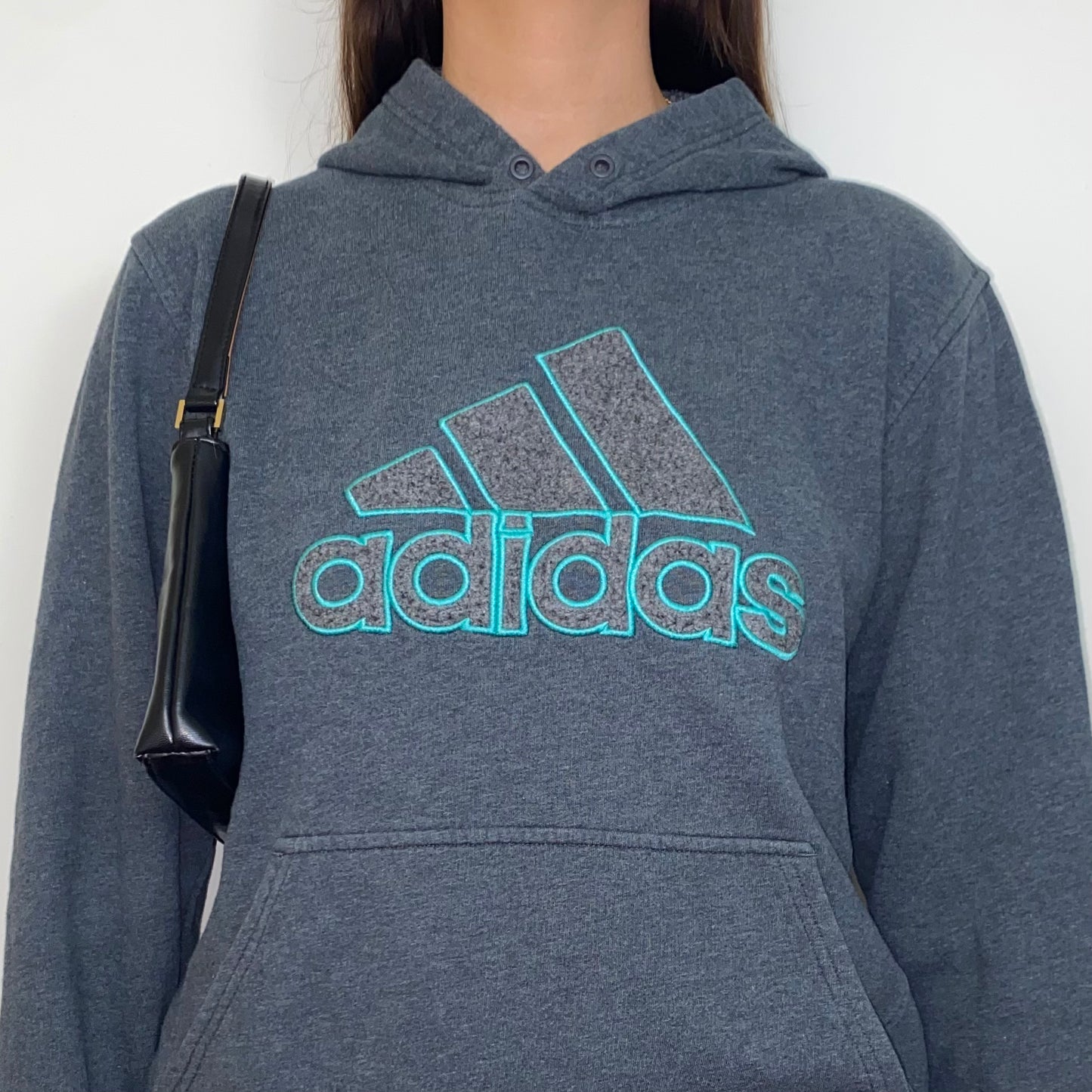 close up of grey hoodie with blue adidas big text logo shown on a model wearing a black shoulder bag