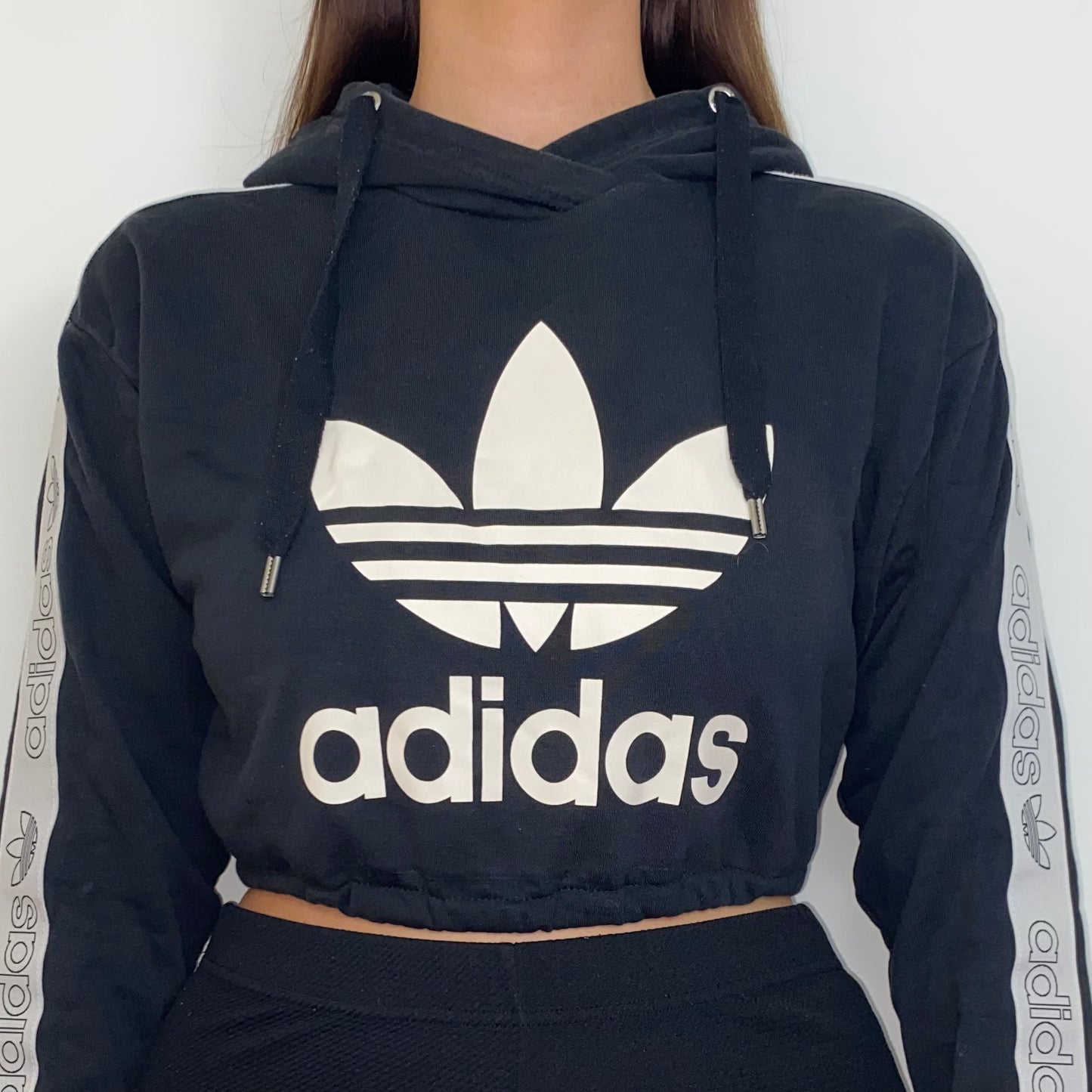 close up of black cropped hoodie with white adidas logo shown on a model
