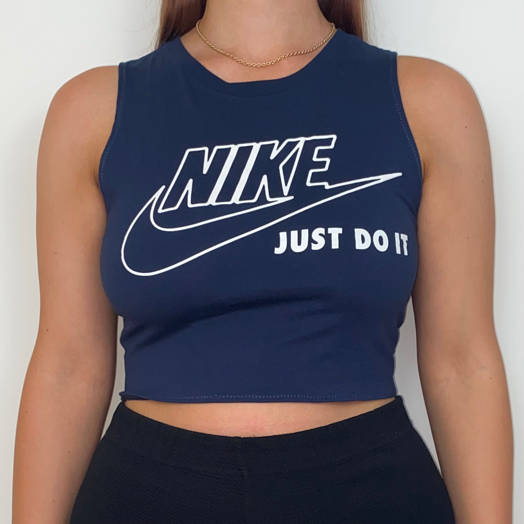 close up of a navy sleeveless crop top with white nike logo shown on a model wearing black trousers