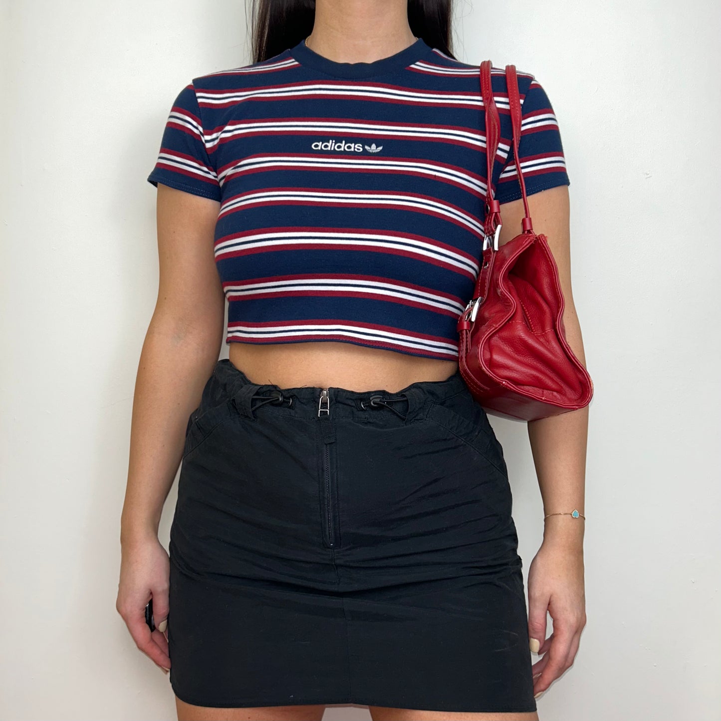 navy and red short sleeve crop top with white adidas logo shown on a model wearing a black mini skirt and red shoulder bag