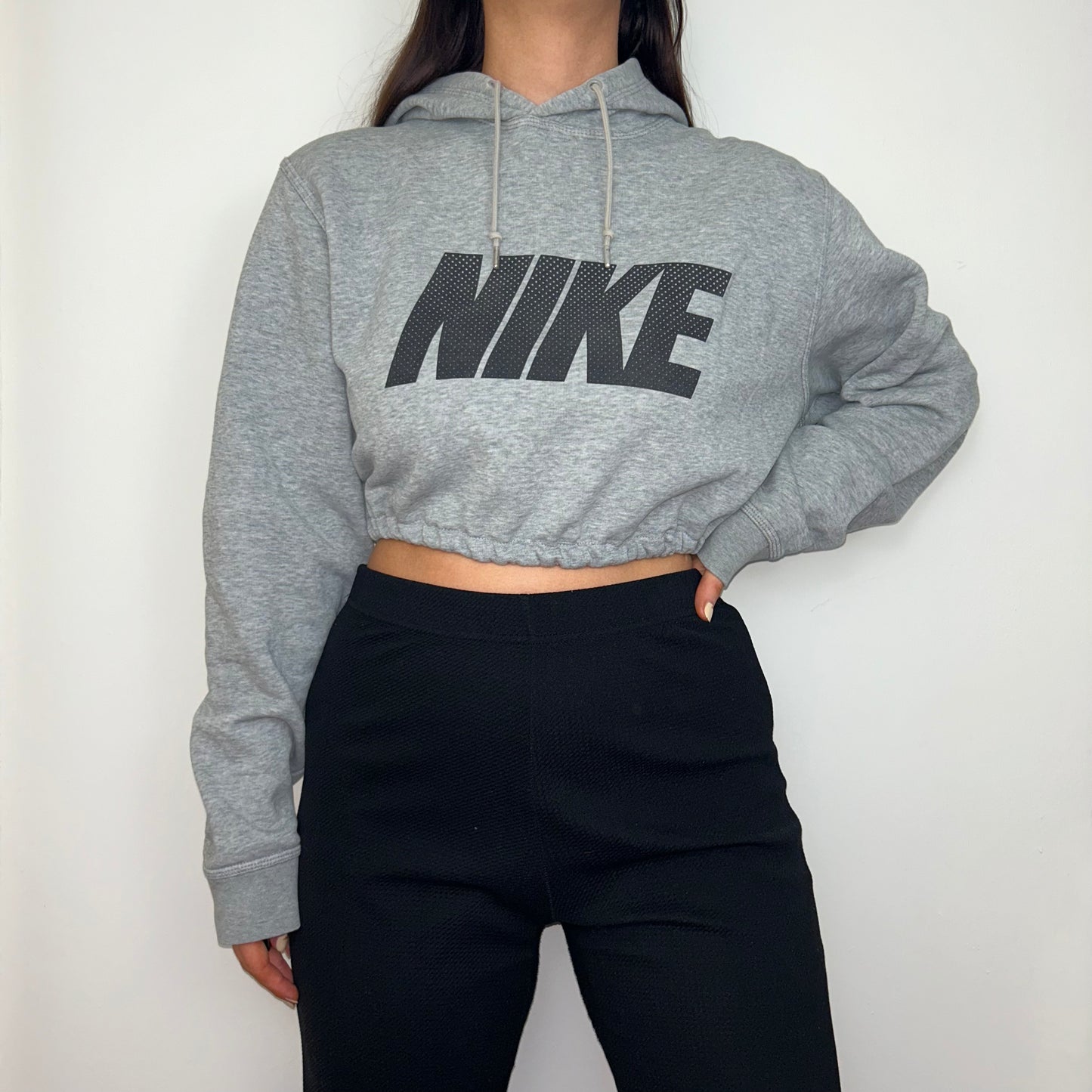 grey cropped hoodie with black nike logo shown on a model wearing black trousers