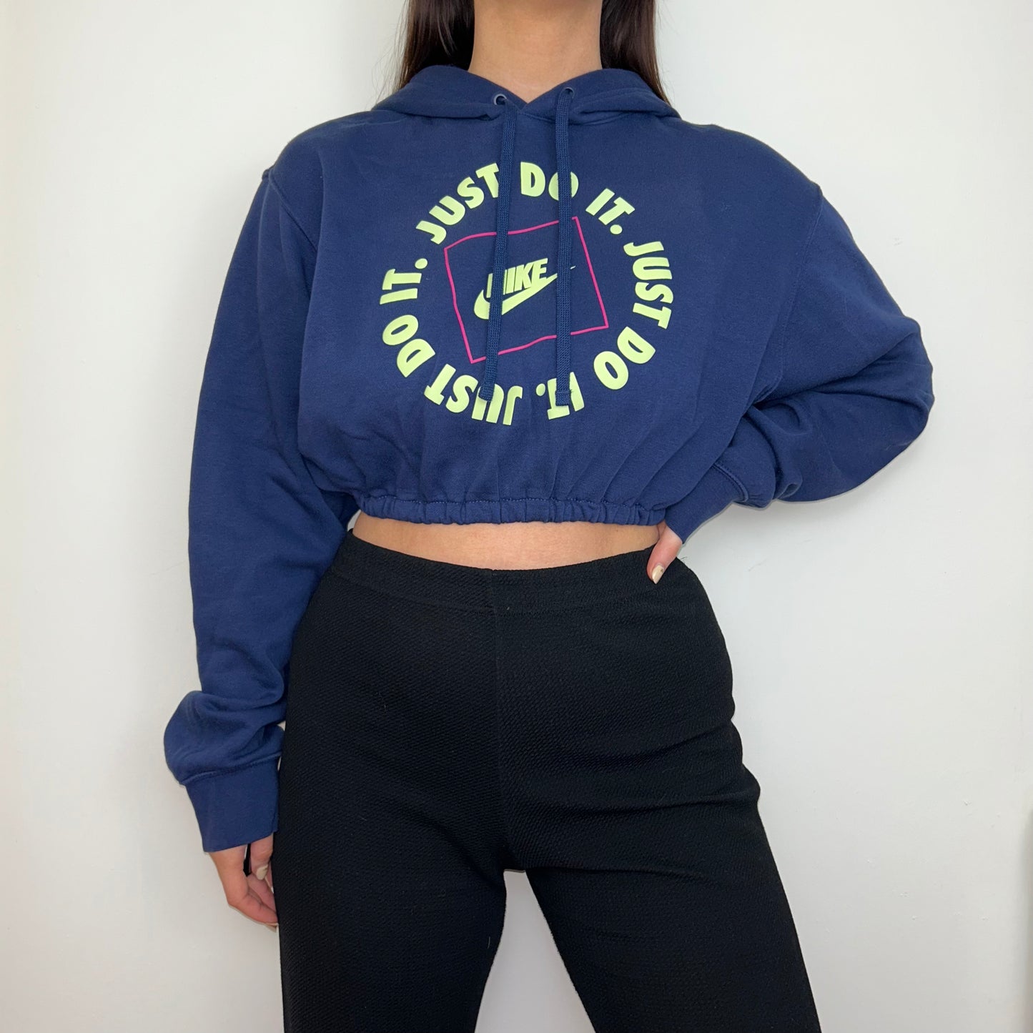 navy blue cropped hoodie with yellow and pink nike text logos shown on a model wearing black trousers