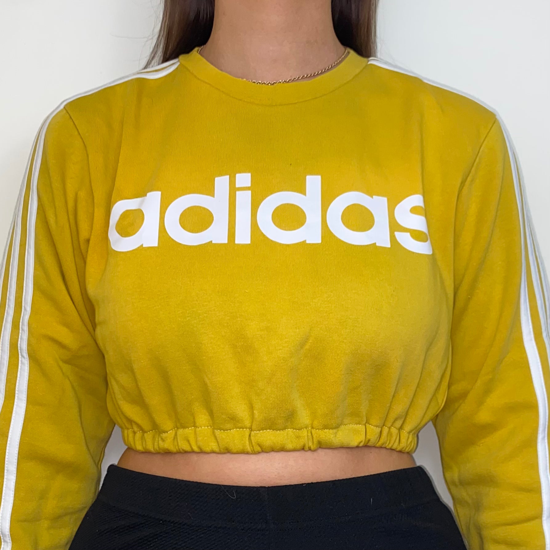 close up of yellow cropped sweatshirt with white adidas logo shown on a model wearing black trousers