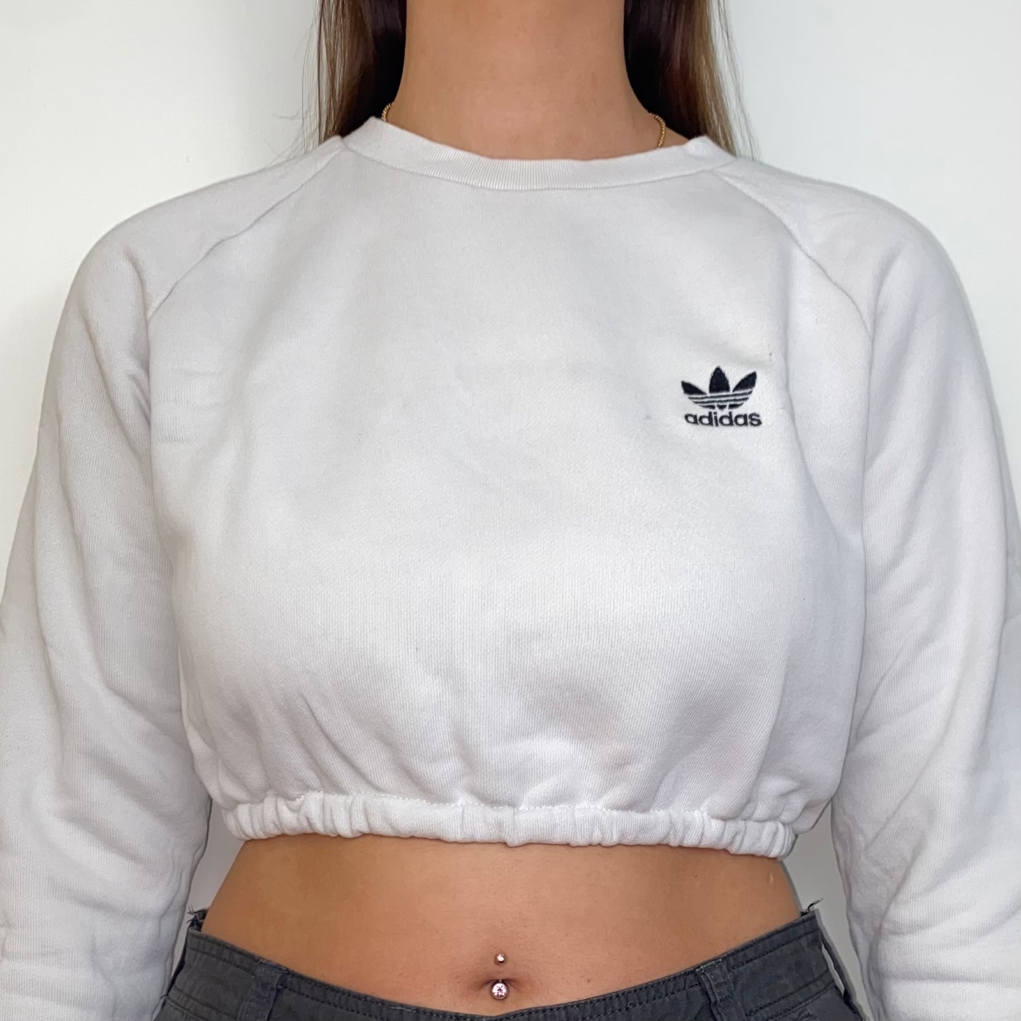 close up of white cropped sweatshirt with black adidas logo shown on a model