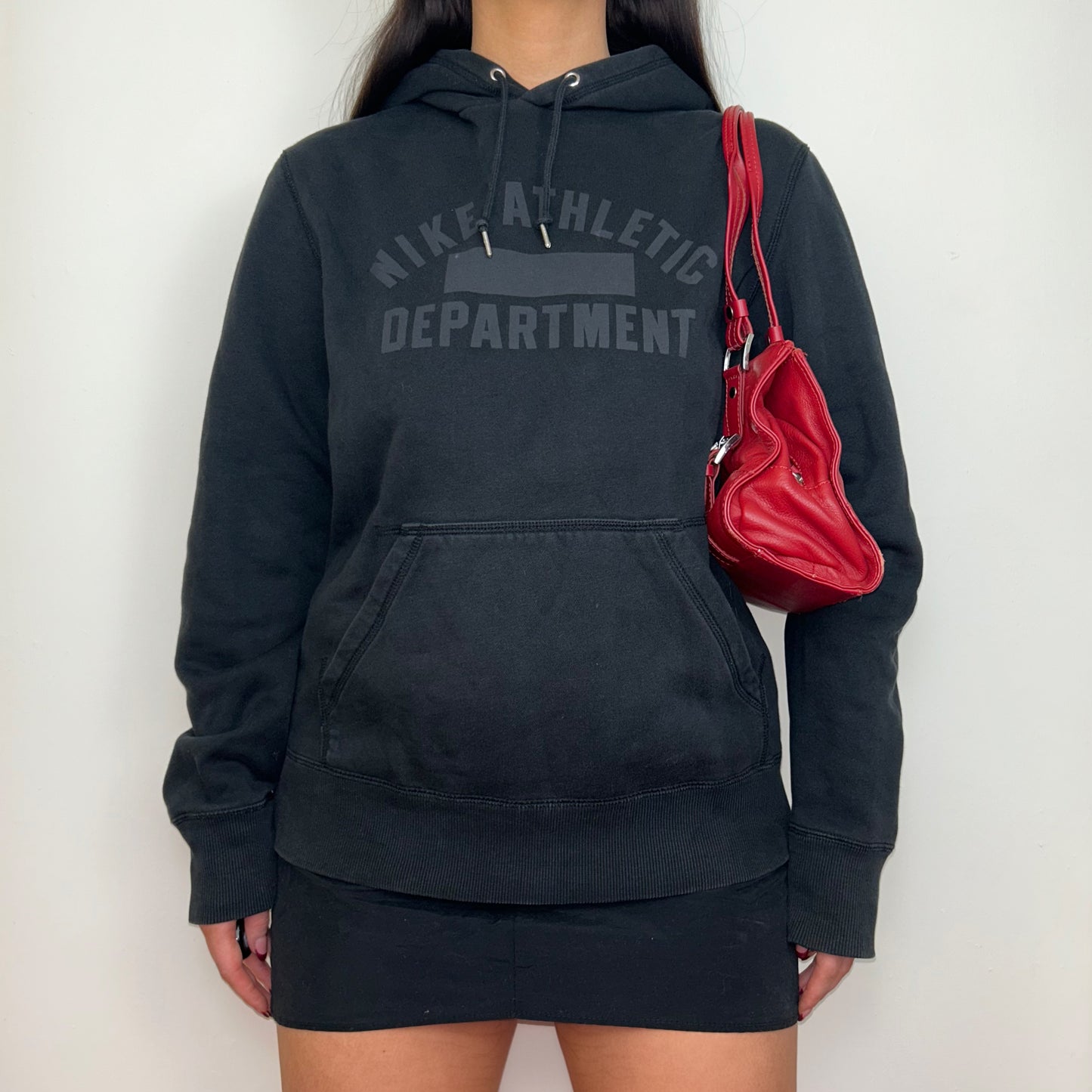 black hoodie with grey nike athletic logo shown on a model wearing a black mini skirt and red shoulder bag