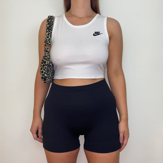 white short sleeve crop top with black nike logo shown on a model wearing black shorts and a leopard print shoulder bag