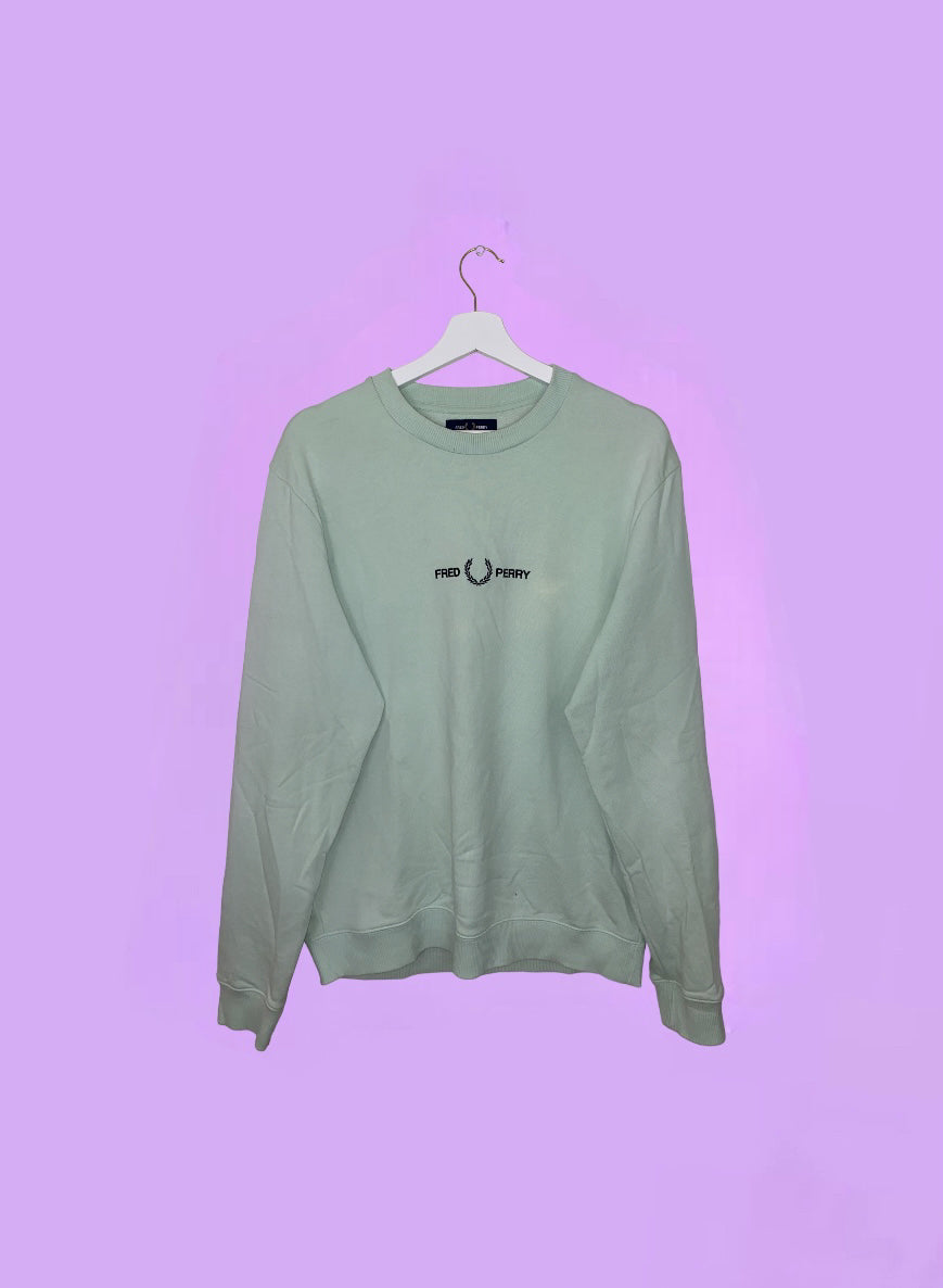green sweatshirt with black fred perry logo shown on a lilac background