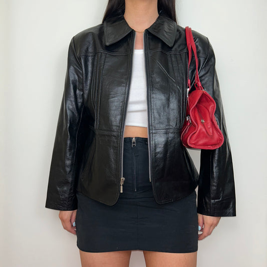 black leather zip up jacket shown on a model wearing a white crop top and black mini skirt with a red shoulder bag