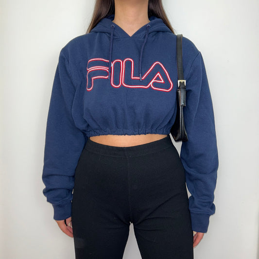navy cropped hoodie with red big text fila logo shown on a model wearing black trousers and a black shoulder bag