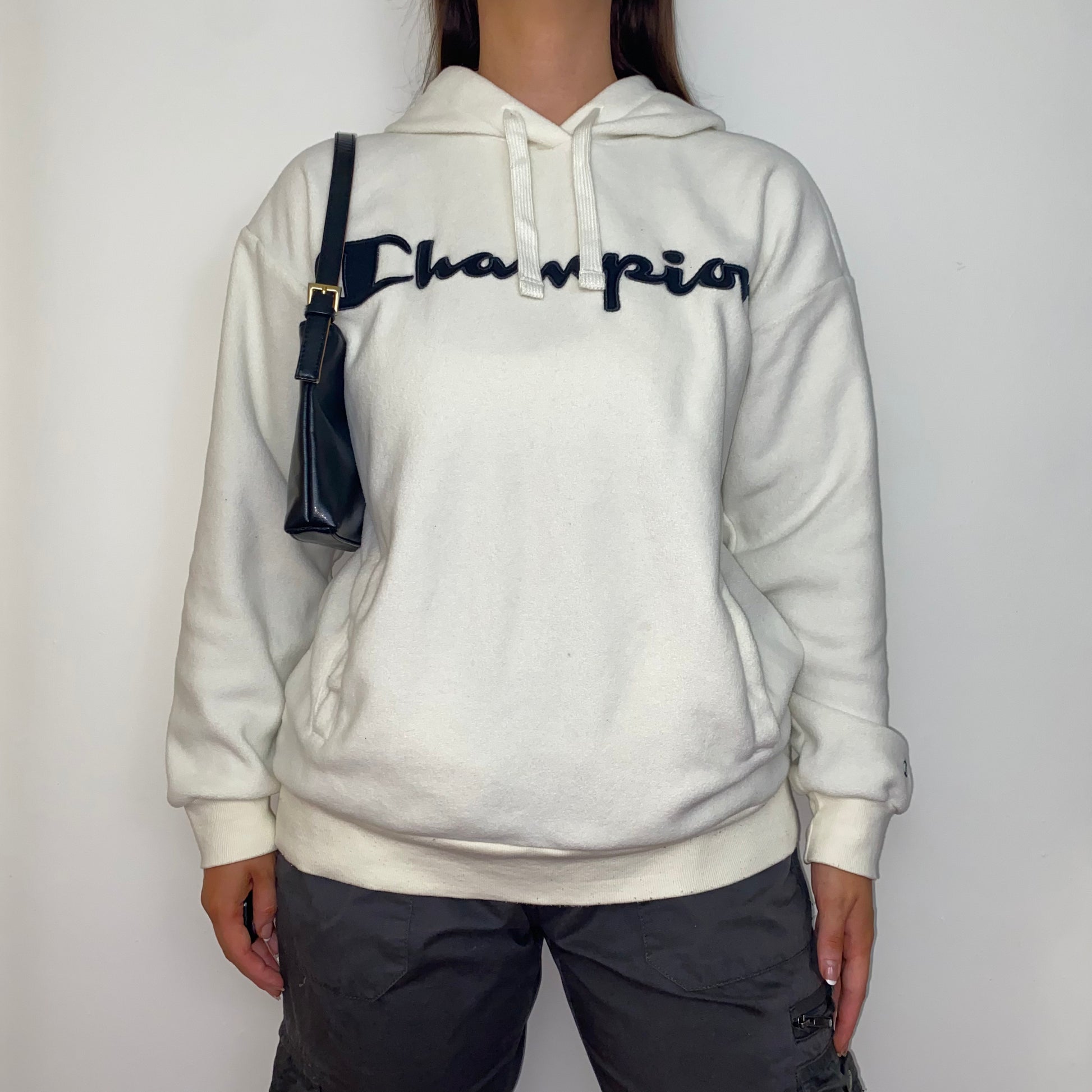 white hoodie with black big text champion logo shown on a model wearing grey cargo trousers and a black shoulder bag
