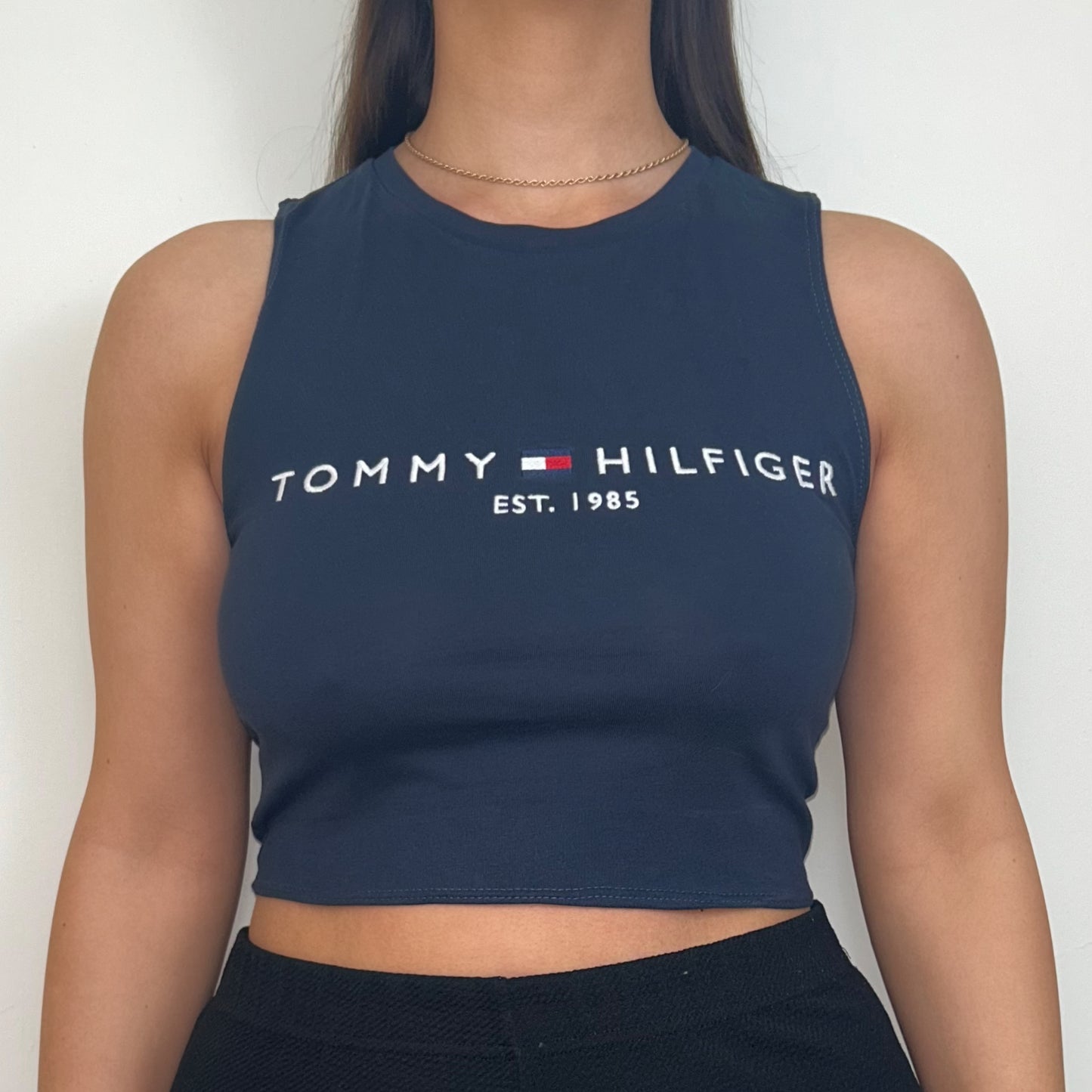 close up of navy sleeveless crop top with white tommy hilfiger logo shown on a model wearing black trousers