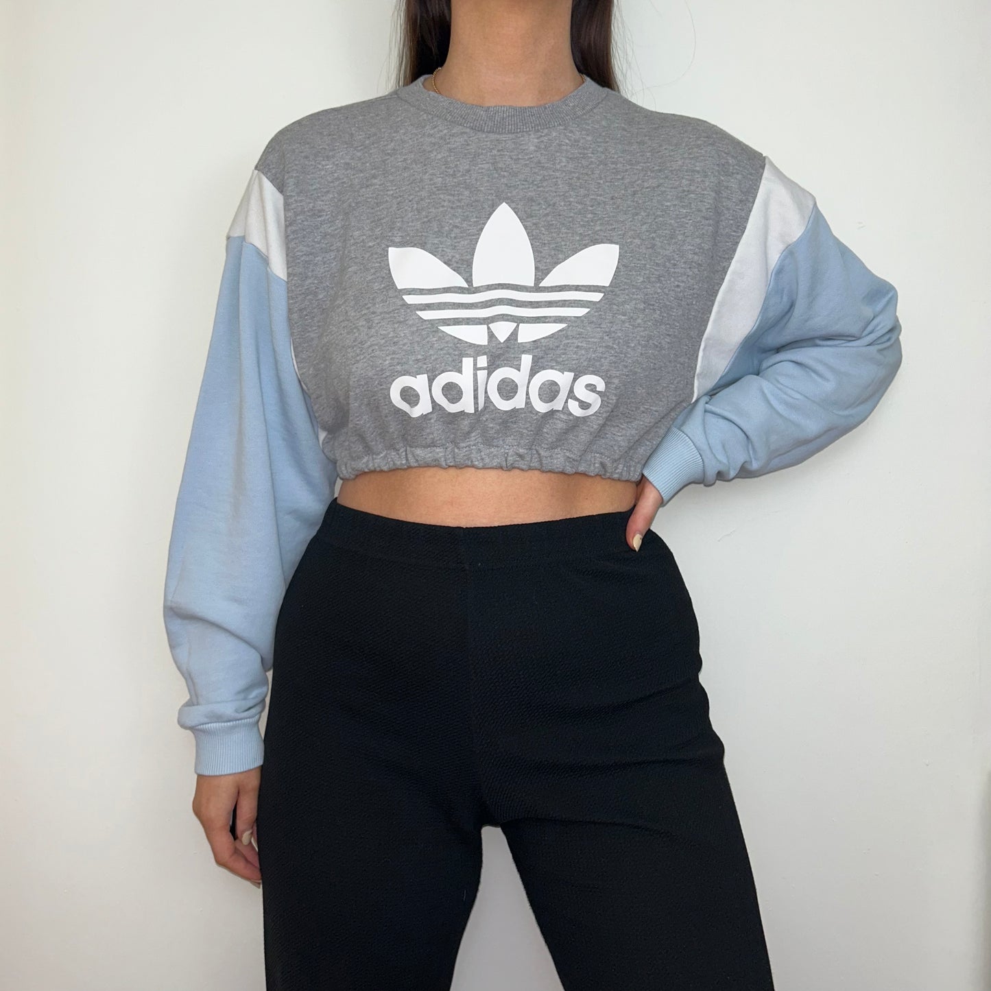 grey and blue cropped sweatshirt with white adidas logo shown on a model wearing black trousers