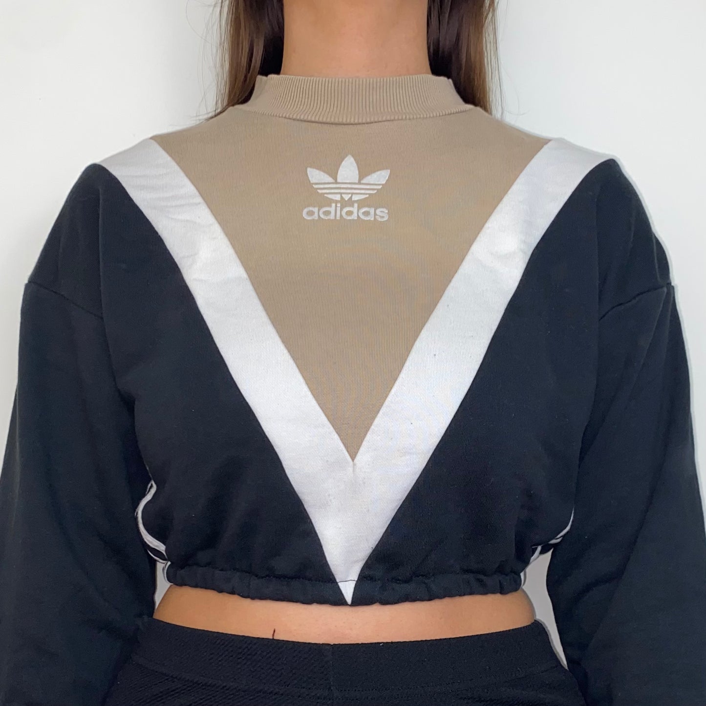 close up of black and beige cropped hoodie with white adidas logo shown on a model wearing black trousers