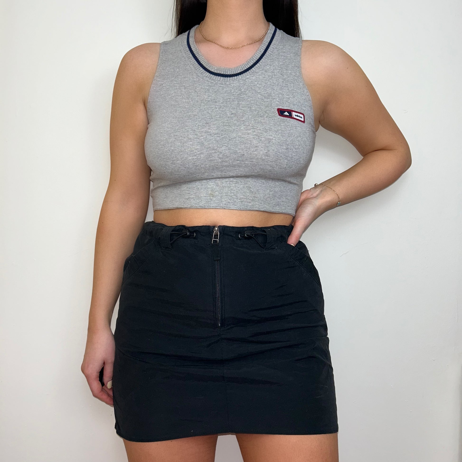 grey sleeveless crop top with small adidas logo shown on a model wearing a black mini skirt