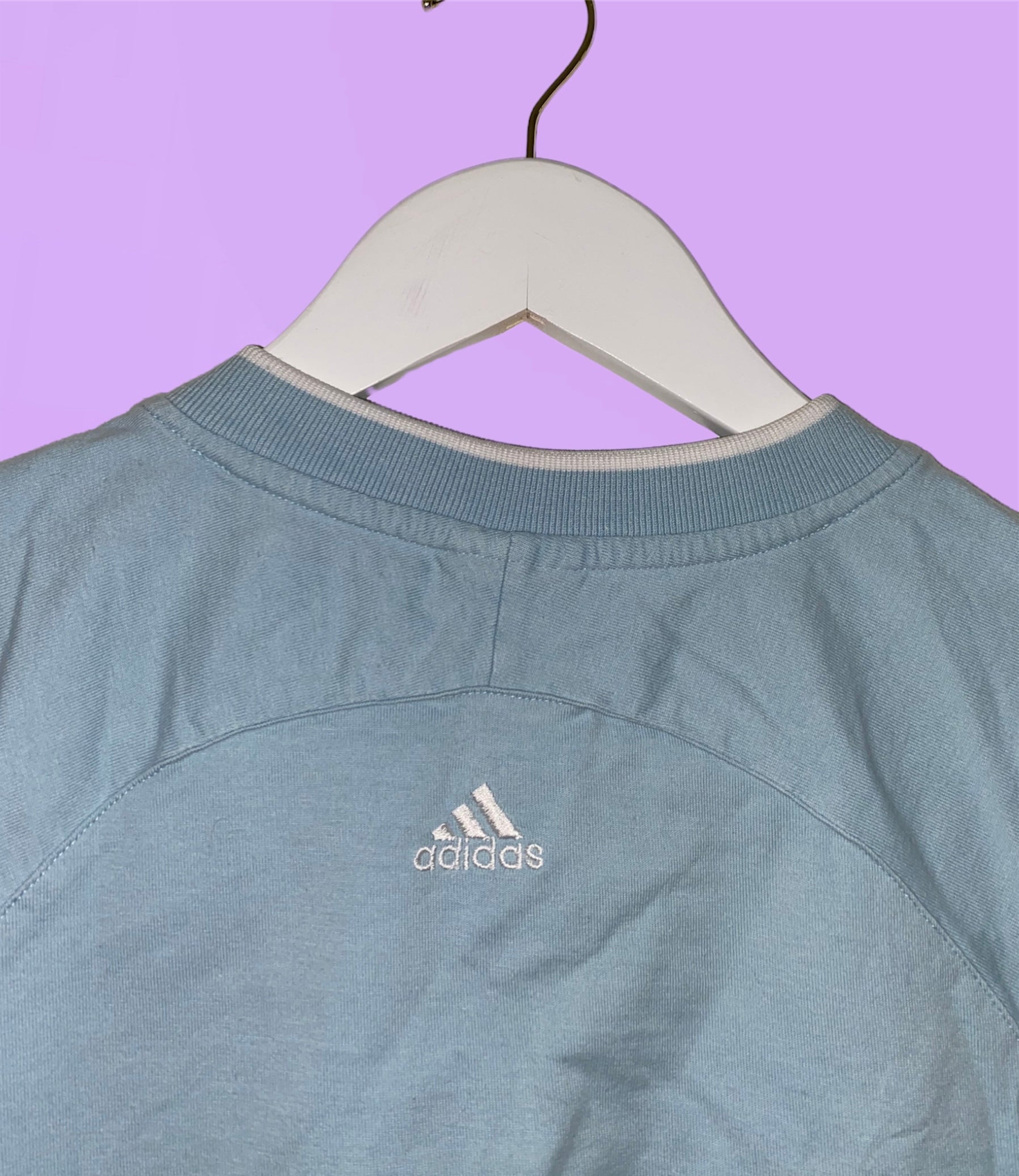 back of a light blue sleeveless crop top with white adidas logo shown on a lilac background