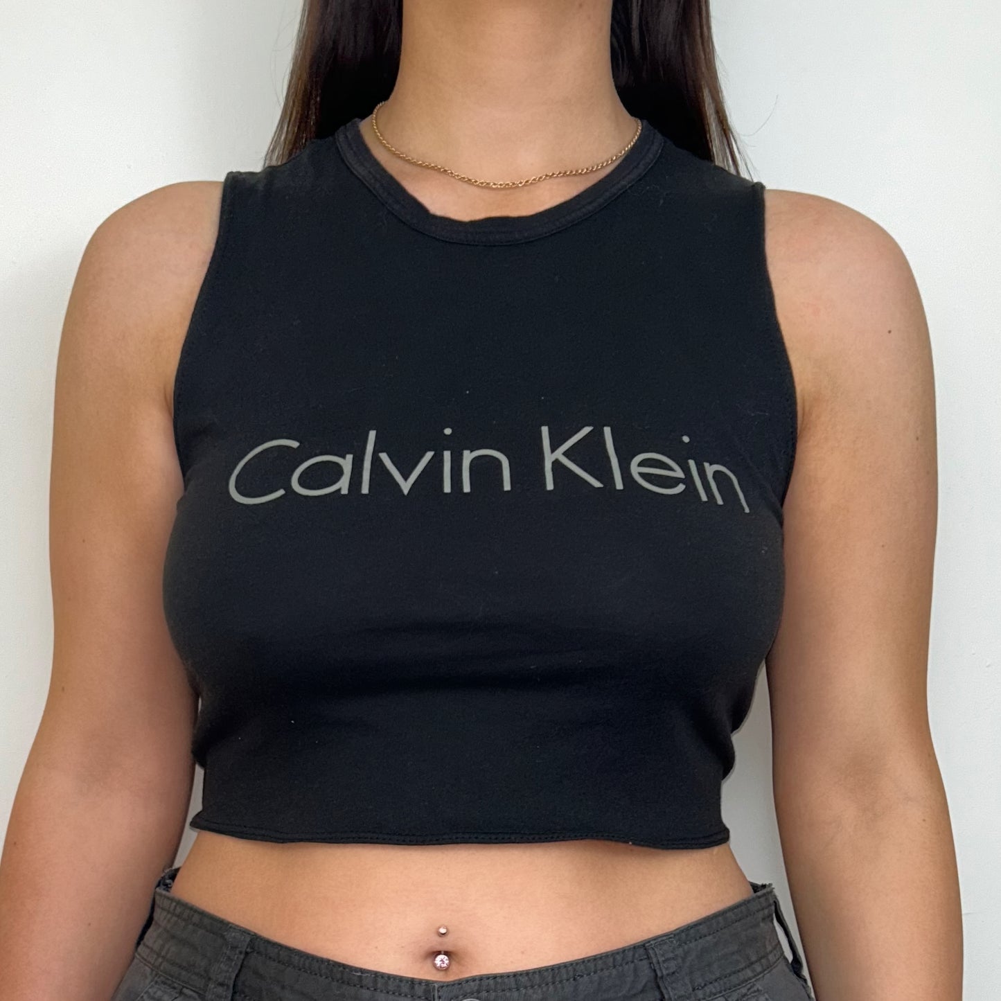 close up of black sleeveless crop top with grey calvin klein logo shown on a model wearing grey cargo trousers