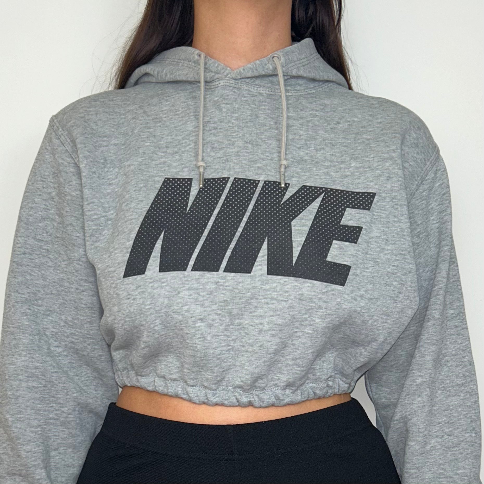 close up of grey cropped hoodie with black nike logo shown on a model wearing black trousers