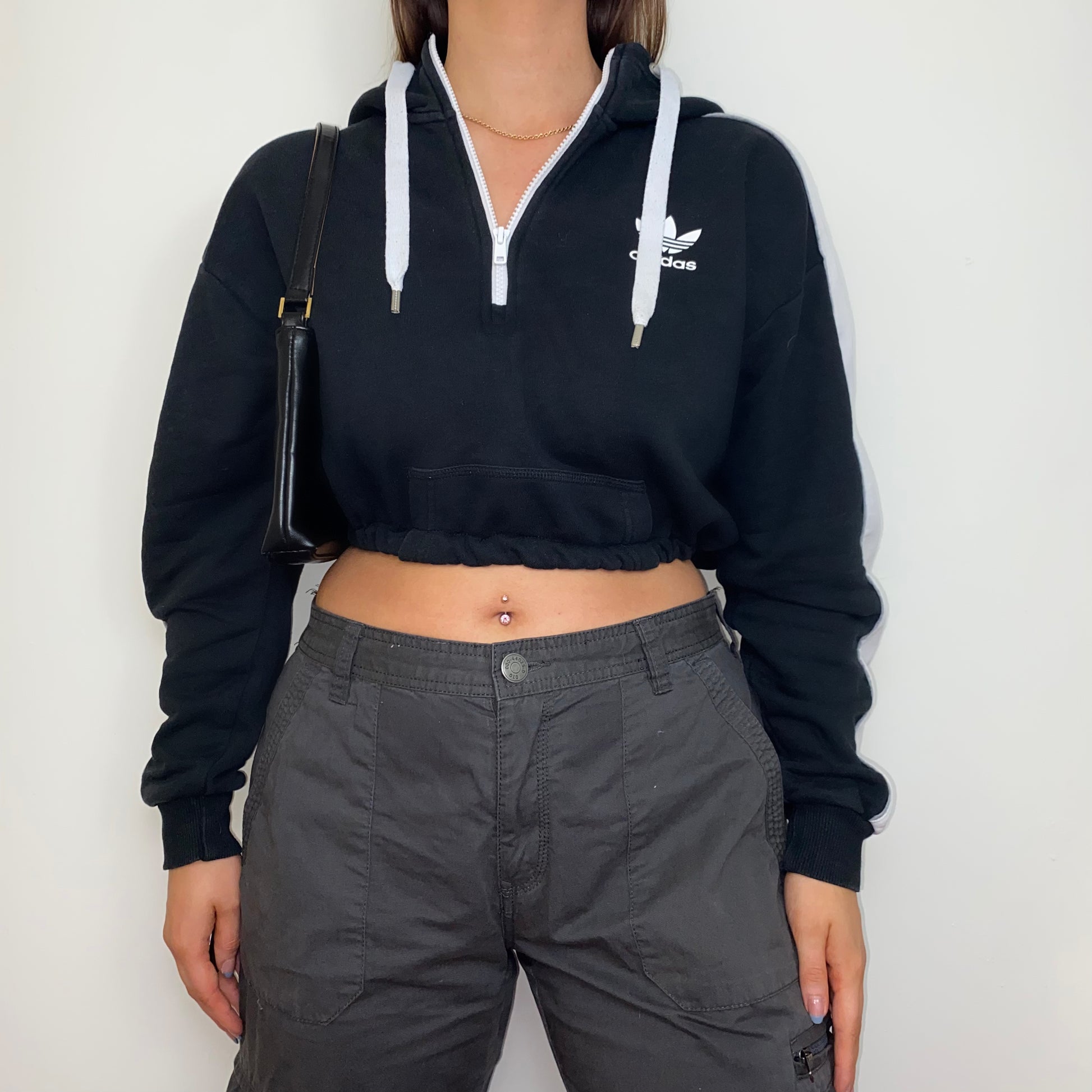 black 1/4 zip cropped hoodie with white adidas logo shown on a model wearing grey cargo trousers with a black shoulder bag