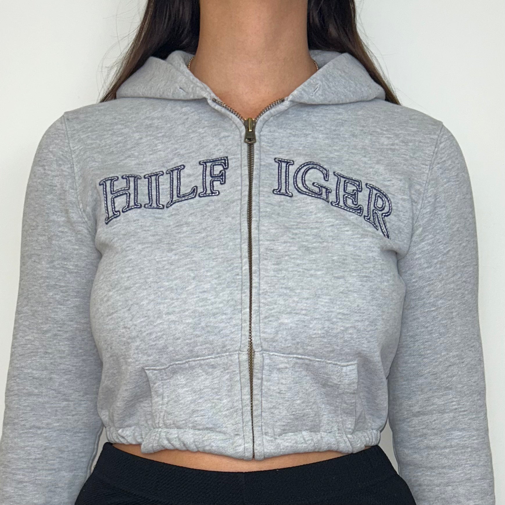 close up of grey 1/4 zip cropped hoodie with navy hilfiger logo shown on a model
