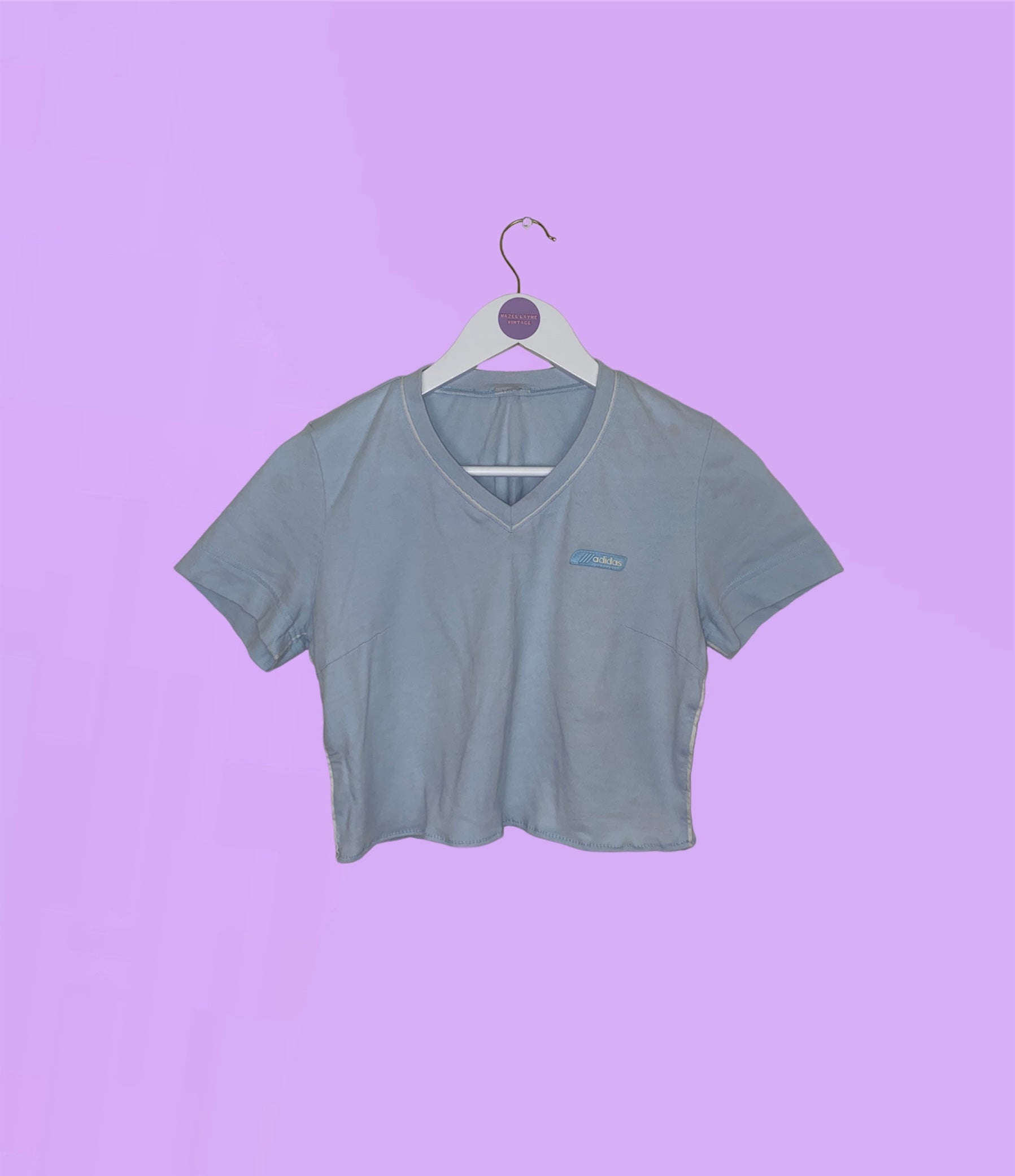 light blue short sleeve crop top with white adidas logo shown on a lilac background