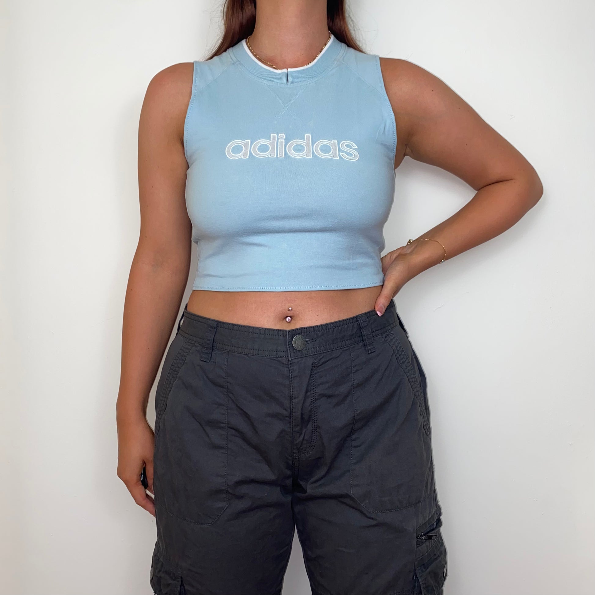 light blue sleeveless crop top with white adidas logo shown on a model wearing grey trousers